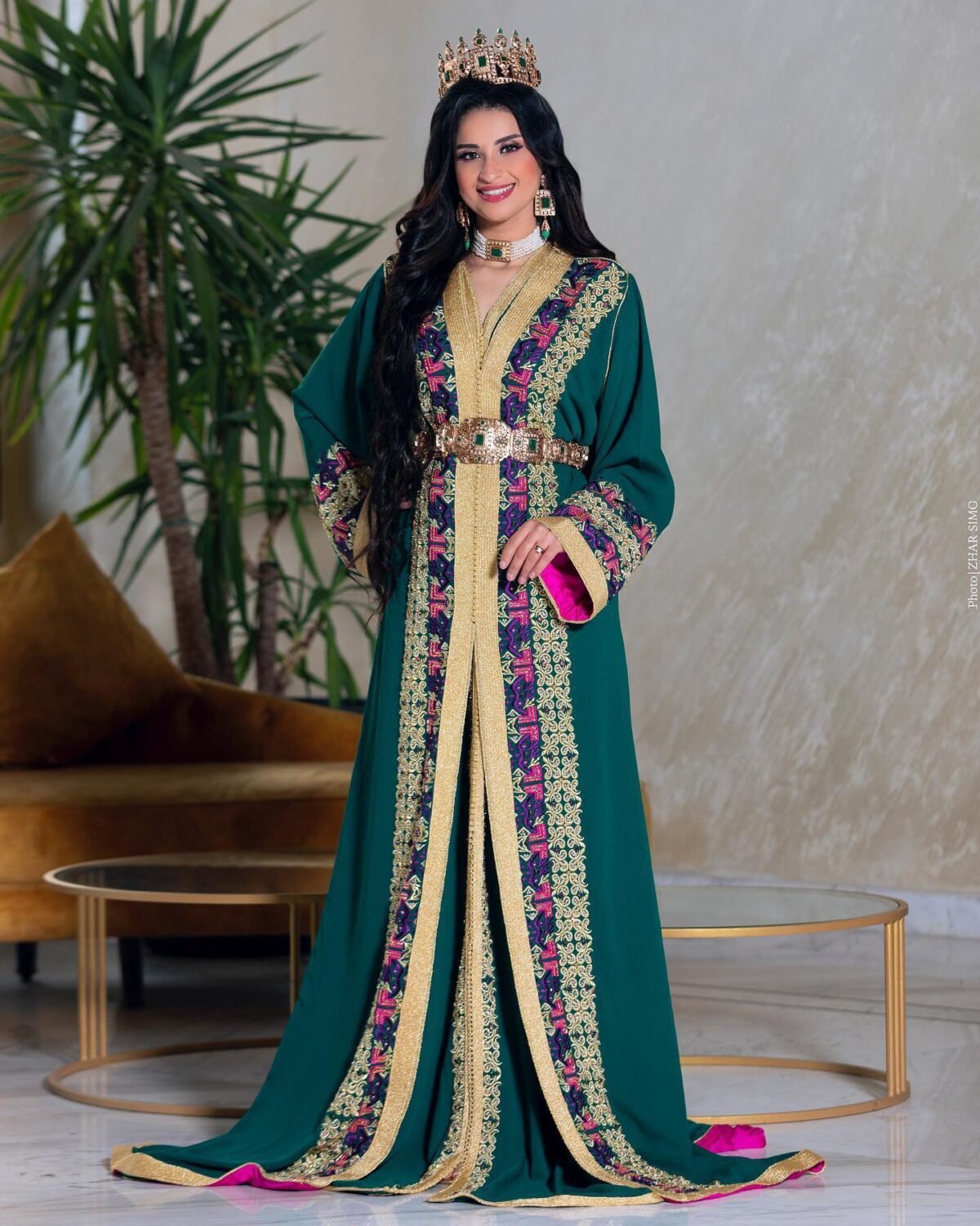 Caftan Market Place Découvrez l'élégance intemporelle du caftan henna, une pièce traditionnelle marocaine magnifiquement ornée. Nos caftans en henna allient beauté et tradition pour des moments inoubliables. Explorez notre collection unique aujourd'hui ! Le caftan Rayhana se compose de deux pièces en crêpe de soie vert, ornées de broderies dorées et rose fushia, de perles en cristal, de sfifa et de boutons en skali doré, doublé en satin de soie fushia. La partie inférieure est confectionnée en drap de soie vert, perlé à la main. Il est accompagné d'une ceinture assortie en métal.